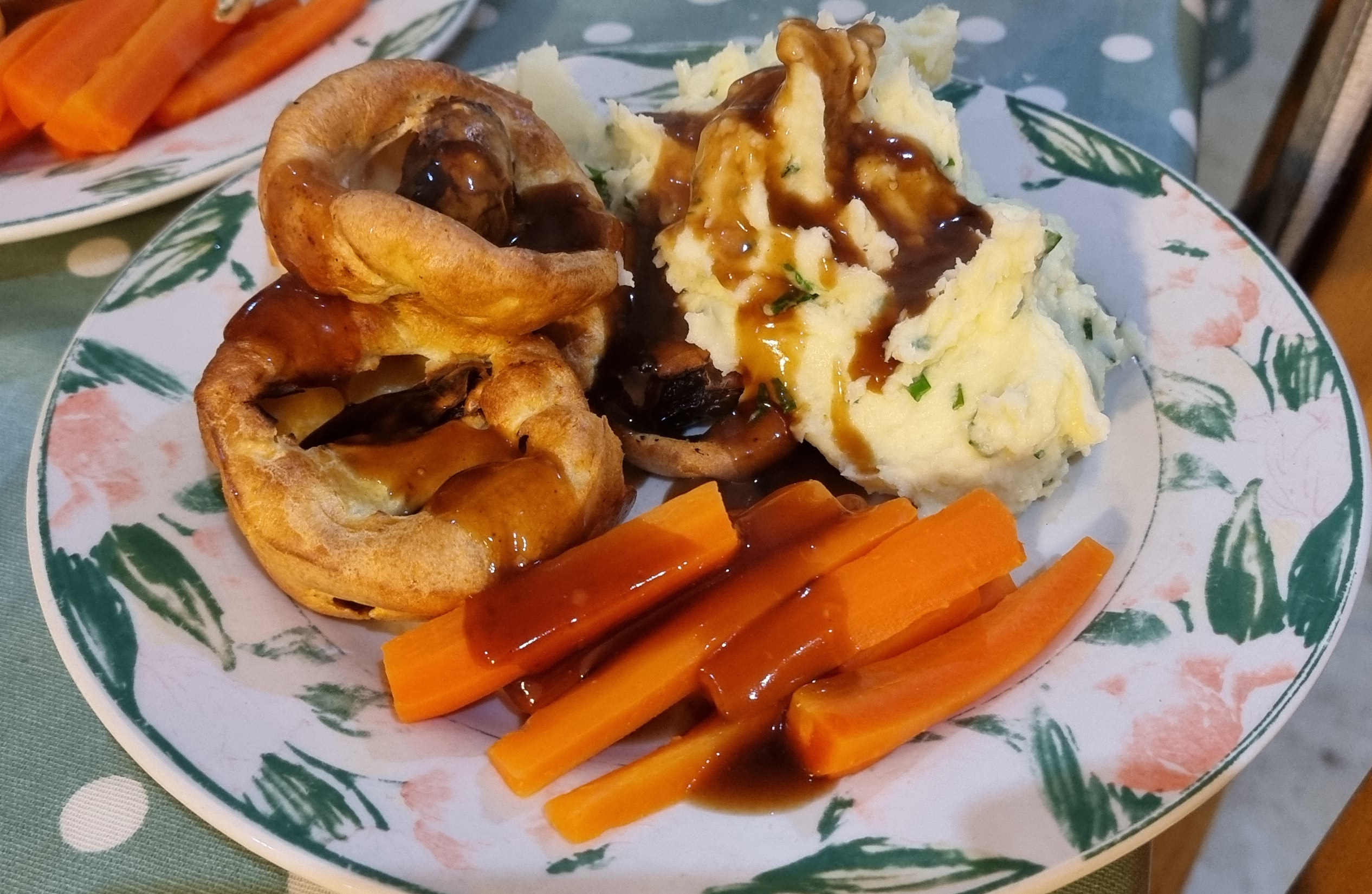 Full image of A pyramid of four bite-sized toads-in-the-hole alongside chive mash and carrots, smothered in gravy, on a plate.
