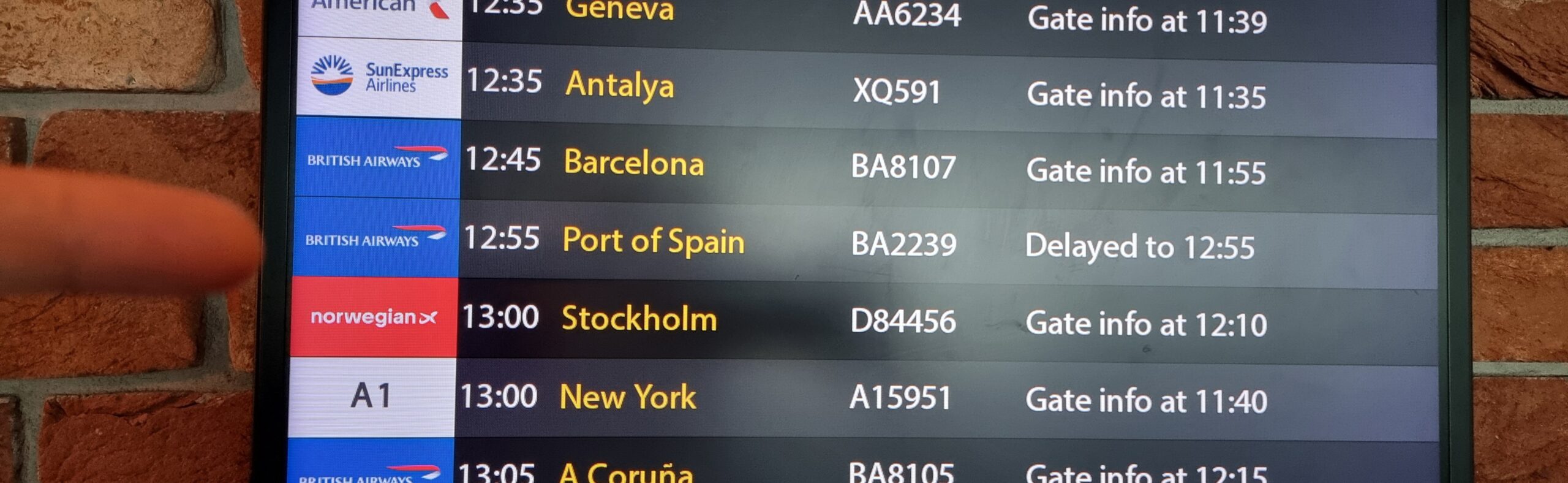 Full image of Airport departures board, showing (among other flights) the 12:55 to Port of Spain is 'Delayed to 12:55'.