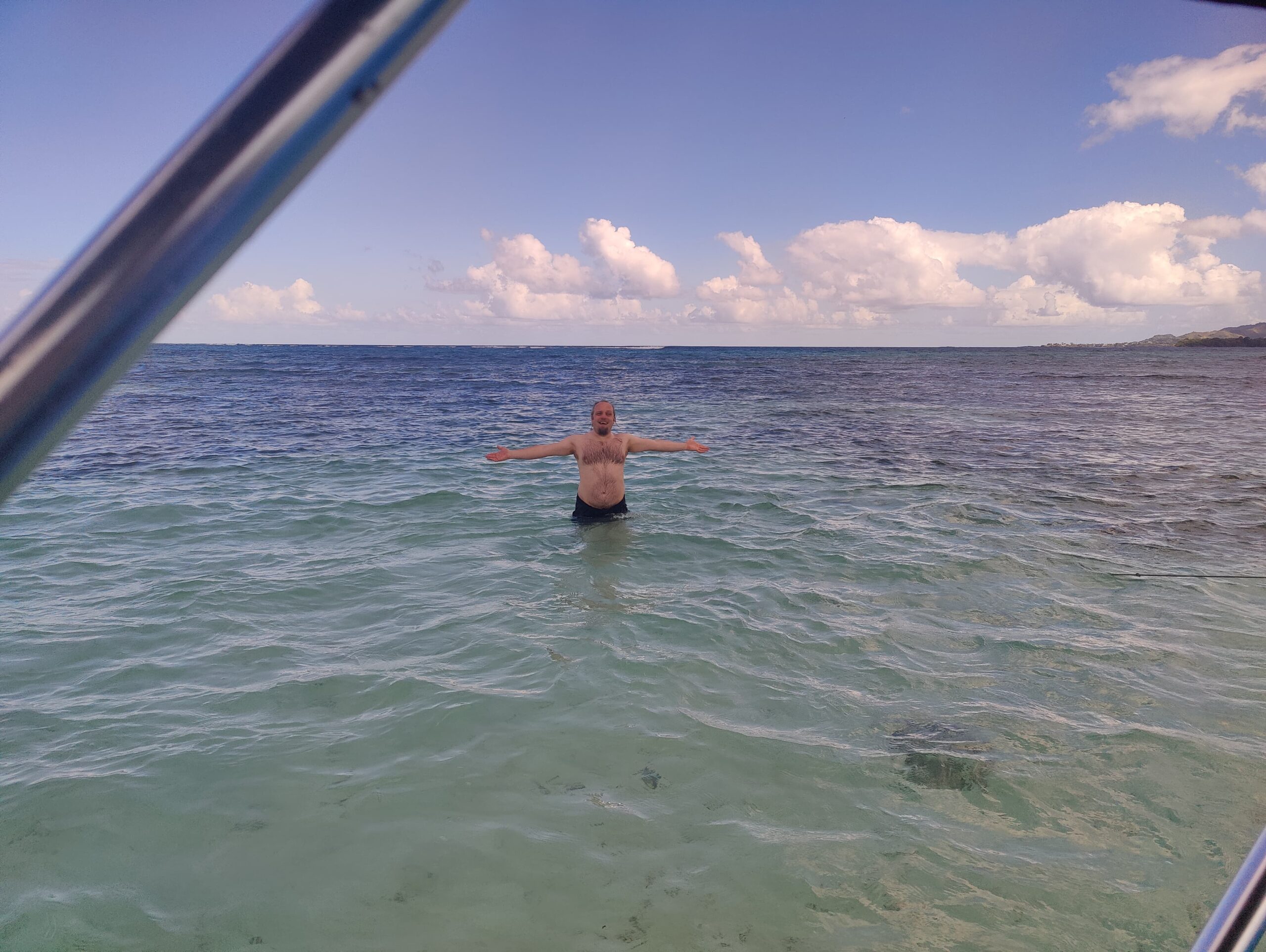 Full image of Dan stands waist-deep in seawater; land is visible in the far distance.