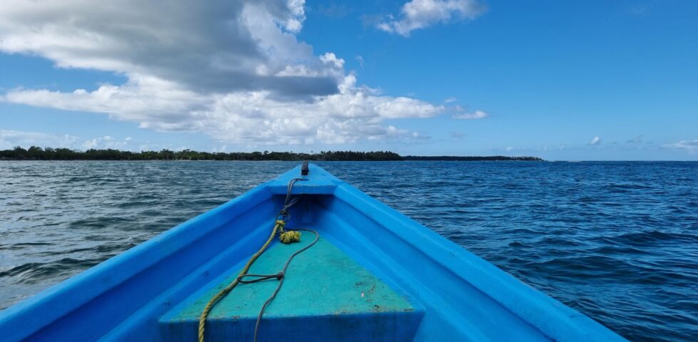 View from the prow of the Cariad, a light blue boat, as she heads towards a distant shore.