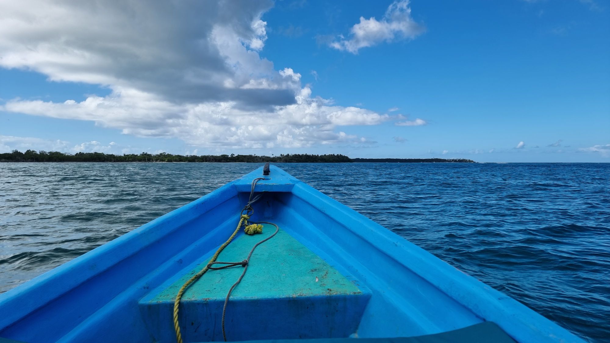 Full image of View from the prow of the Cariad, a light blue boat, as she heads towards a distant shore.