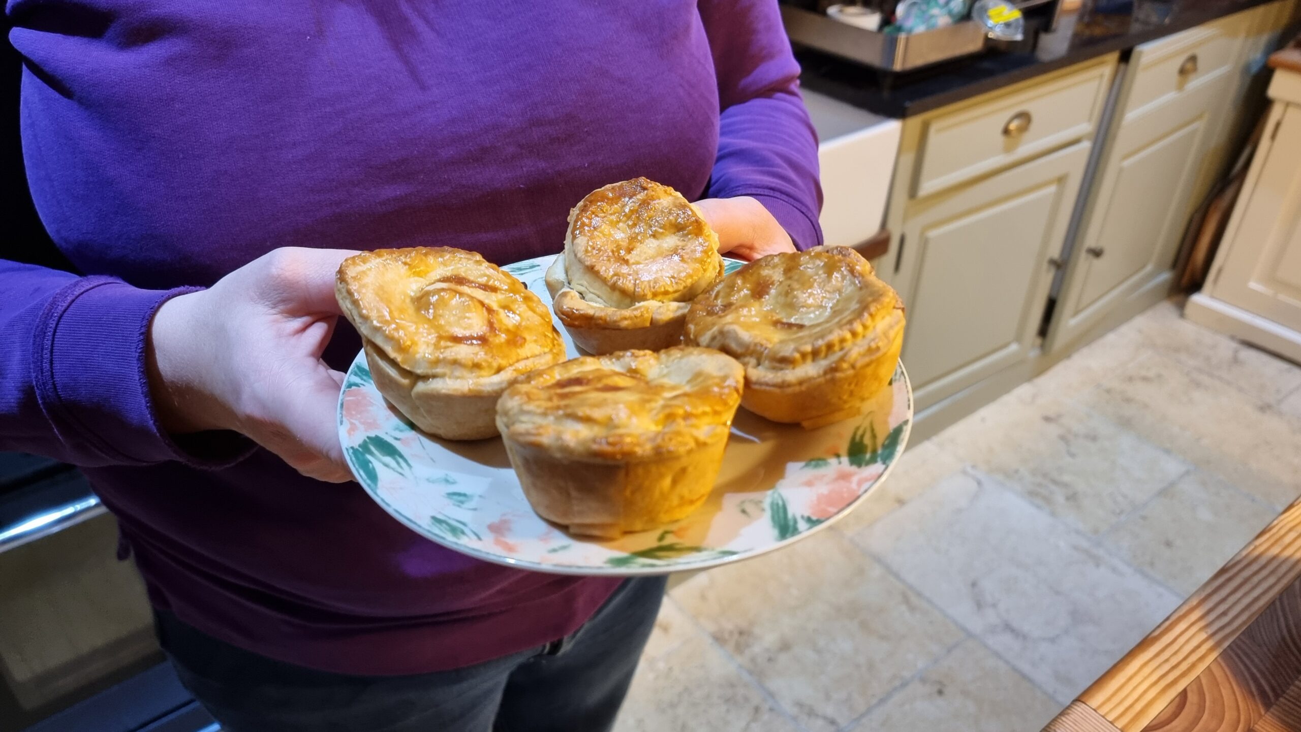 Full image of Plate containing four beautifully-browned but slightly lopsided pies, held in a woman's hands.