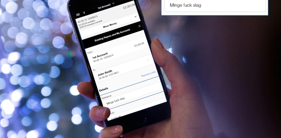 Mobile phone, held in a white person's hand, showing an online banking screenshot: a payment to John Smith is being configured, with the reference set as "Minge fuck slag".