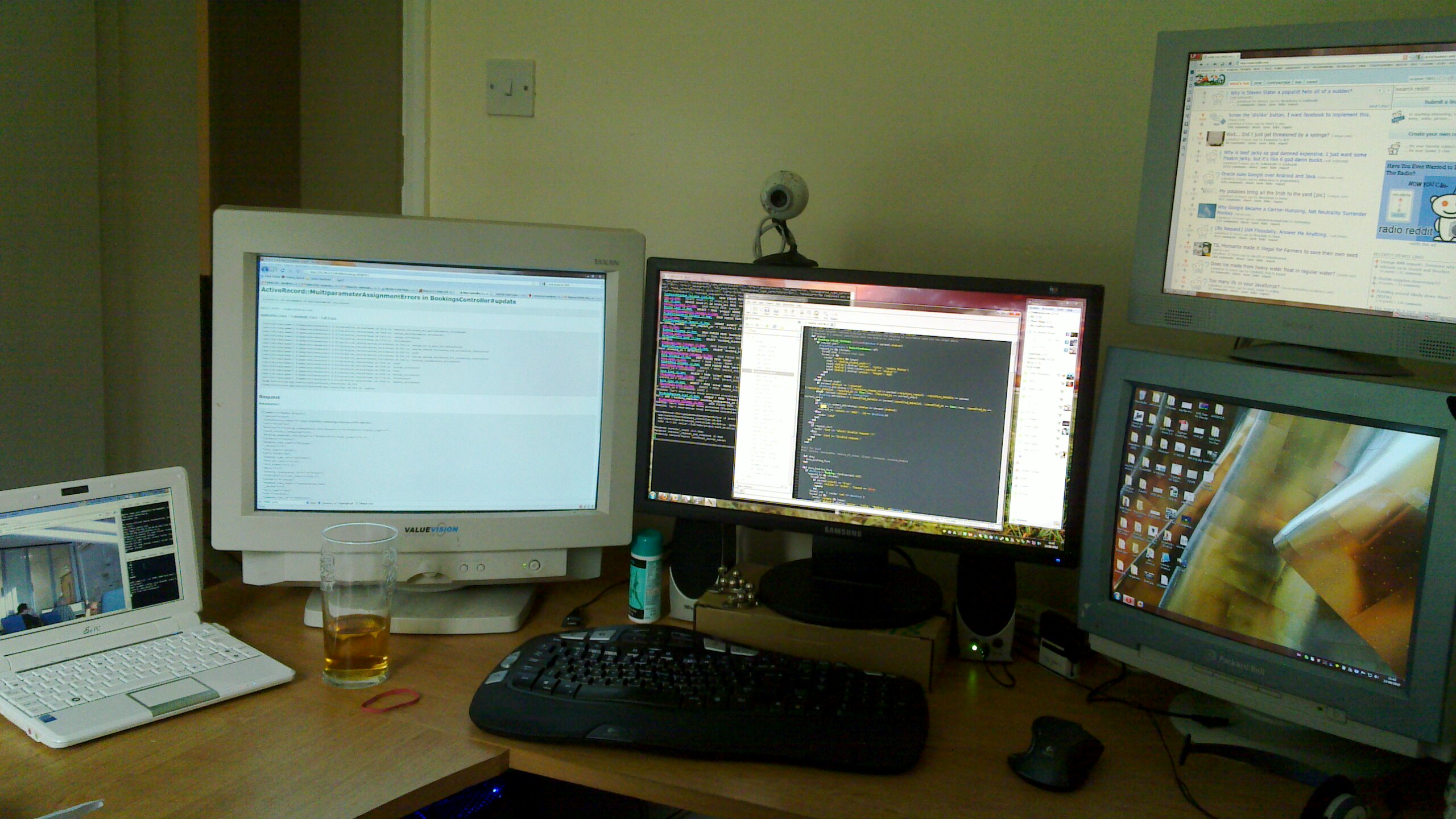 Full image of A mixture of flatscreen and CRT monitors, plus a laptop and a webcam, on a desk. The laptop screen shots a view of an office at the "other end" of a webcam connection.