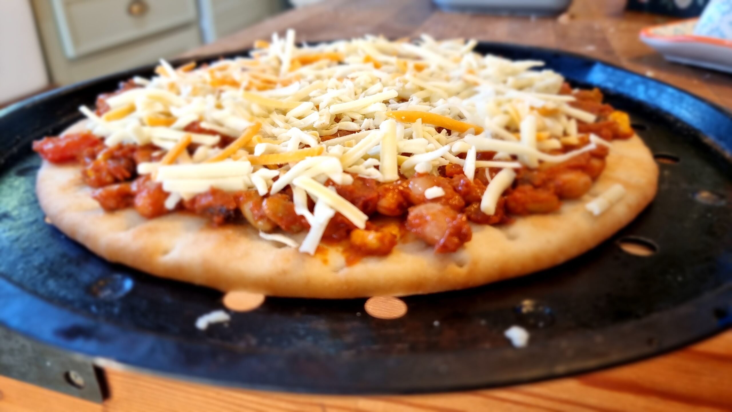 Full image of Pizza built with bean chilli and mixed grated cheese, ready to go into an oven.