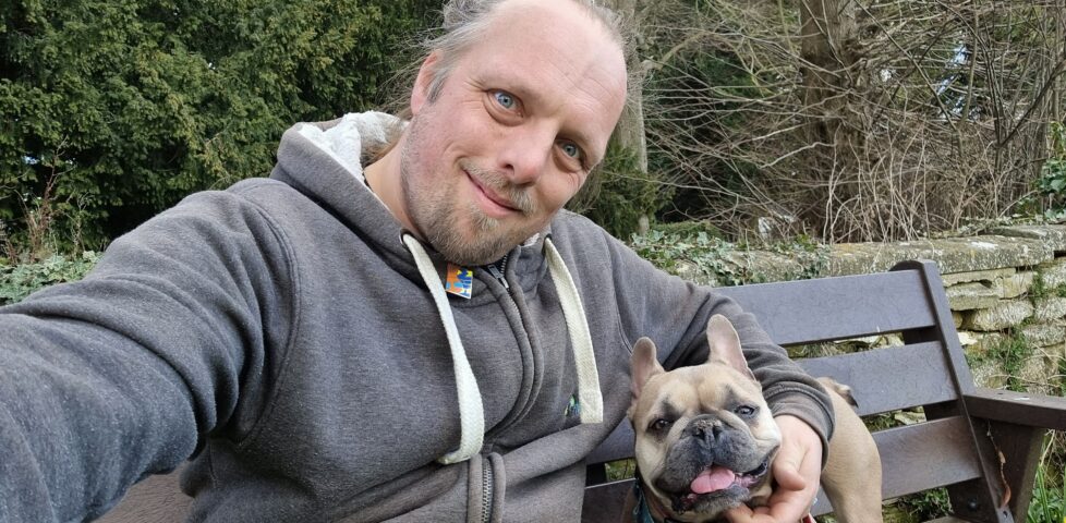 Dan and his dog sit on a bench outside a churchyard.