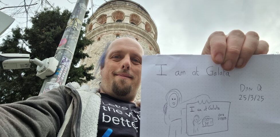 In front of the Galata Tower, Dan holds up a sign that reads 'I am at Galata' and depicts him holding up a sign that reads 'I am at Galata' and depicts him holding up a sign, and so on...