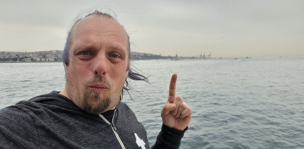 Dan stands and takes a selfie while pointing to a distant tower, protruding from water off the shore of Asian Istanbul.