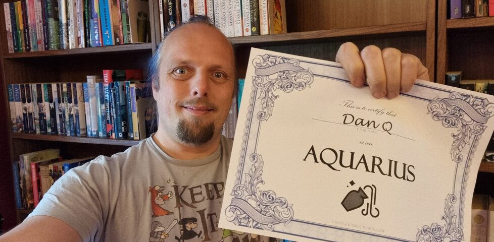 Dan, in a library, smiles as he holds up a certificate that certifies that he is an Aquarius.