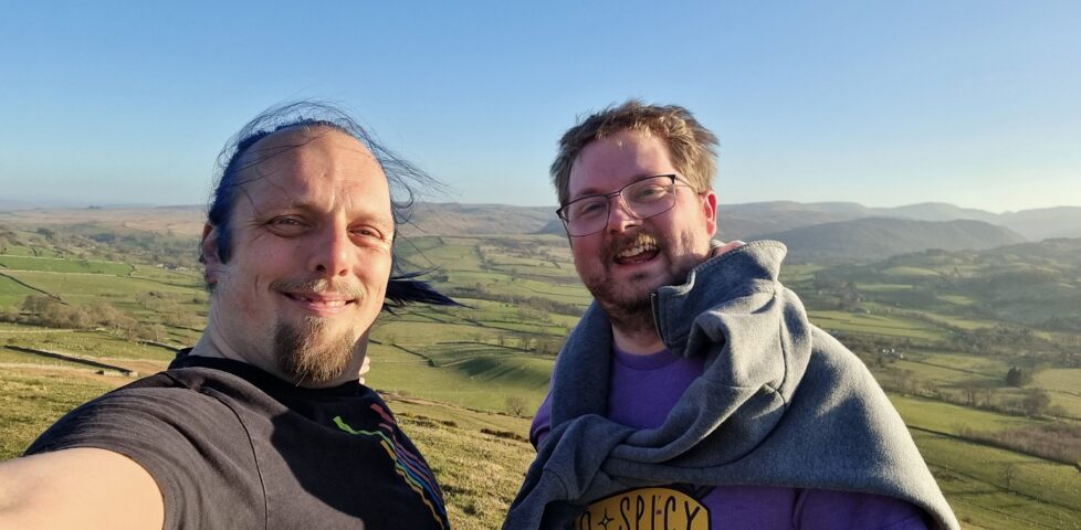 Two white men stand on a windy Lake District hilltop.