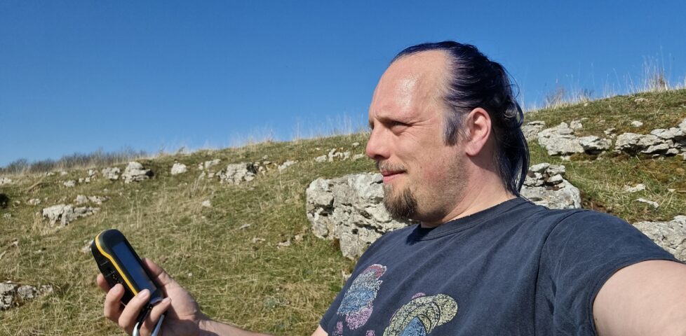 Dan examines his GPSr on a sun-drenched craggy hillside.