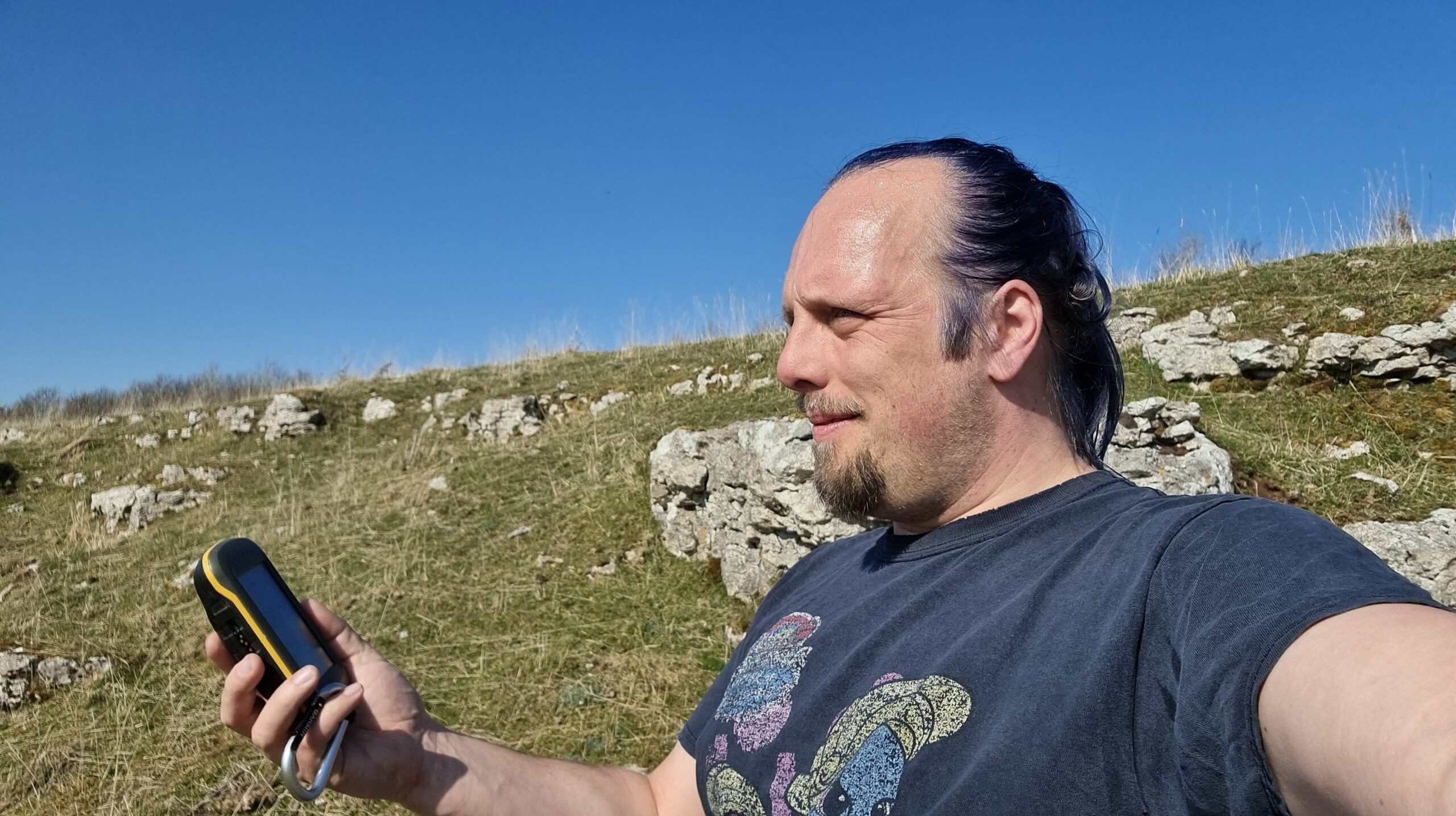Full image of Dan examines his GPSr on a sun-drenched craggy hillside.