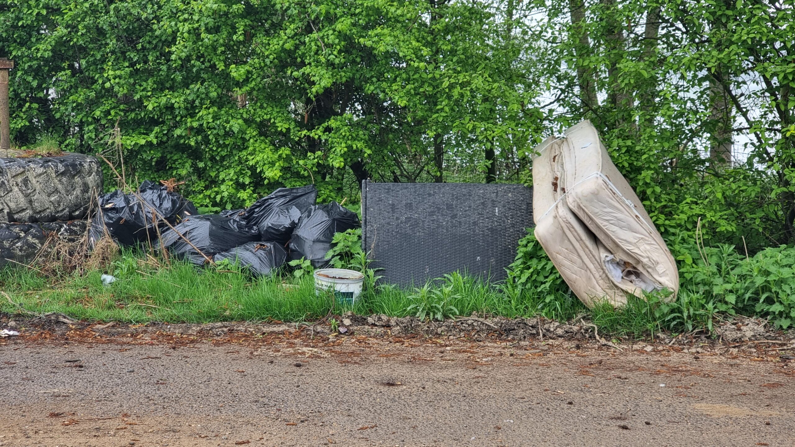 Full image of A fly-tipped mattress and bin bags in a layby.