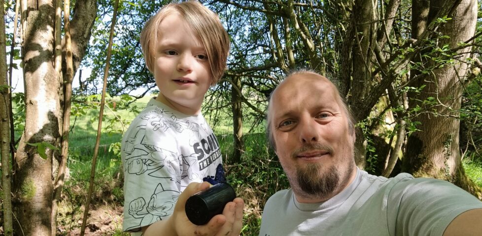 Dan crouches alongside an 8-year-old boy in a forest.