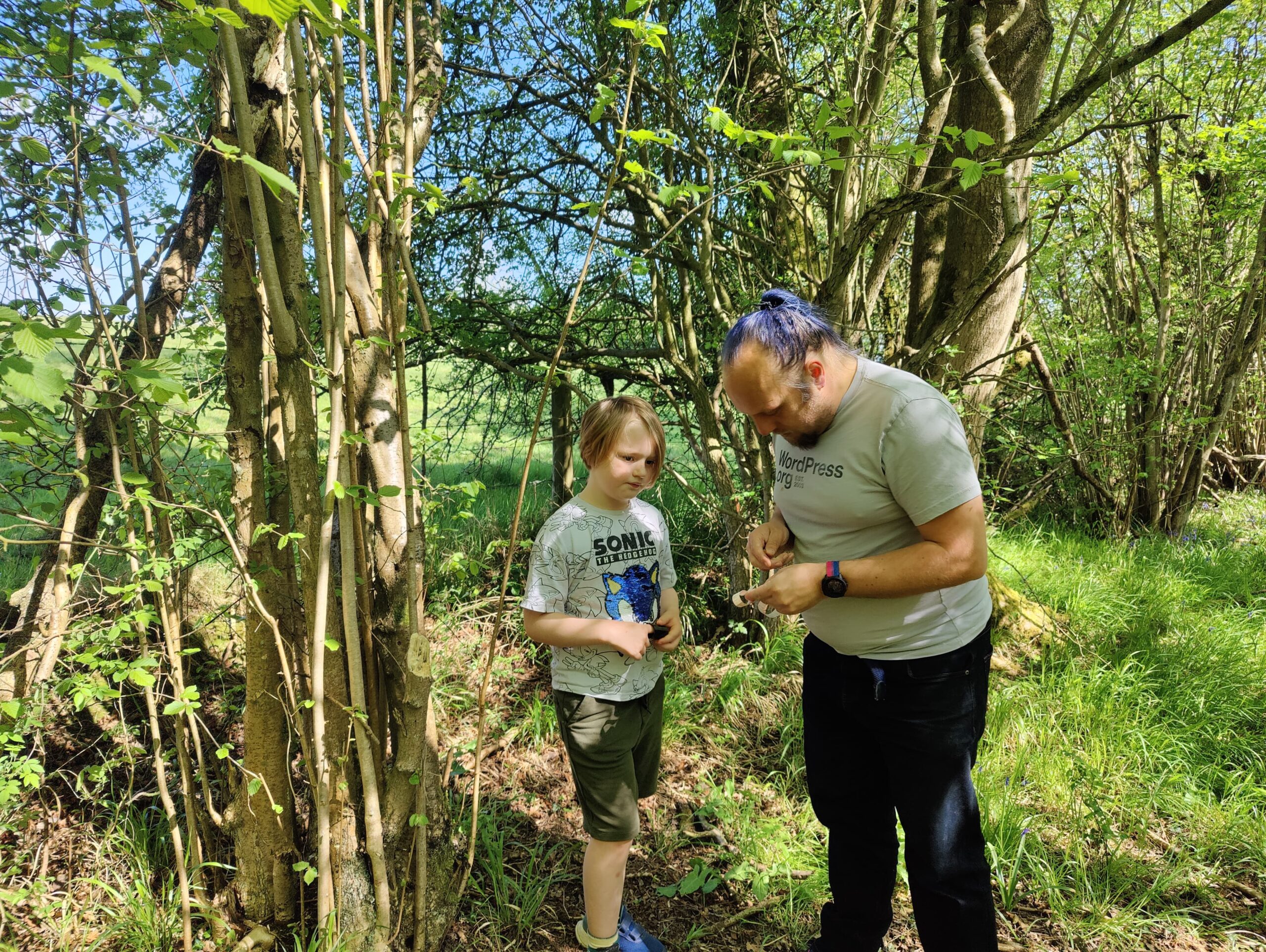 Full image of Dan helps a child open a small geocache container, in a forest.