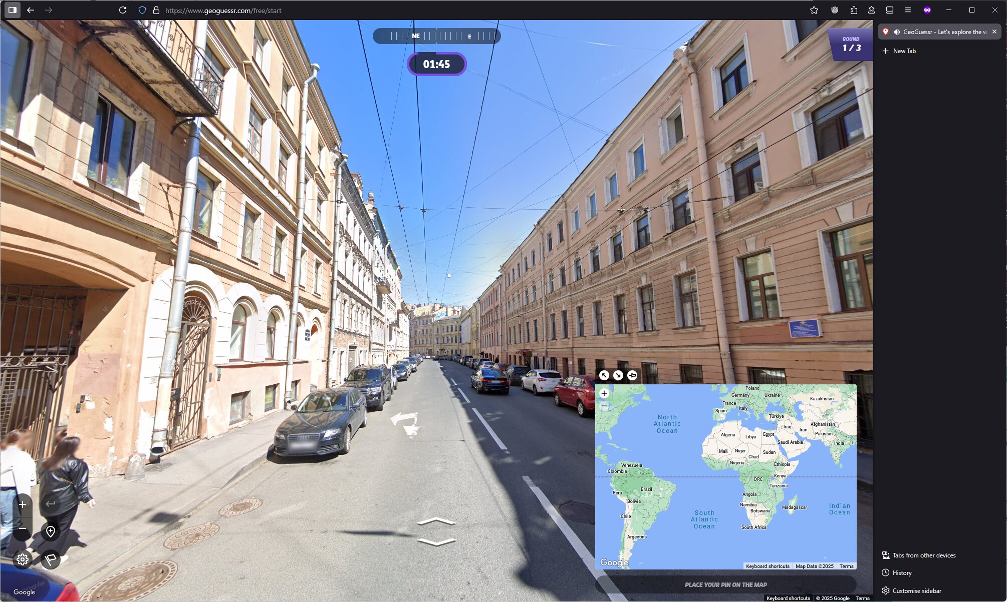 Full image of City street shown in GeoGuessr, with white and cream buildings, under a bright blue sky. 1 minute 45 seconds remains to place a pin.