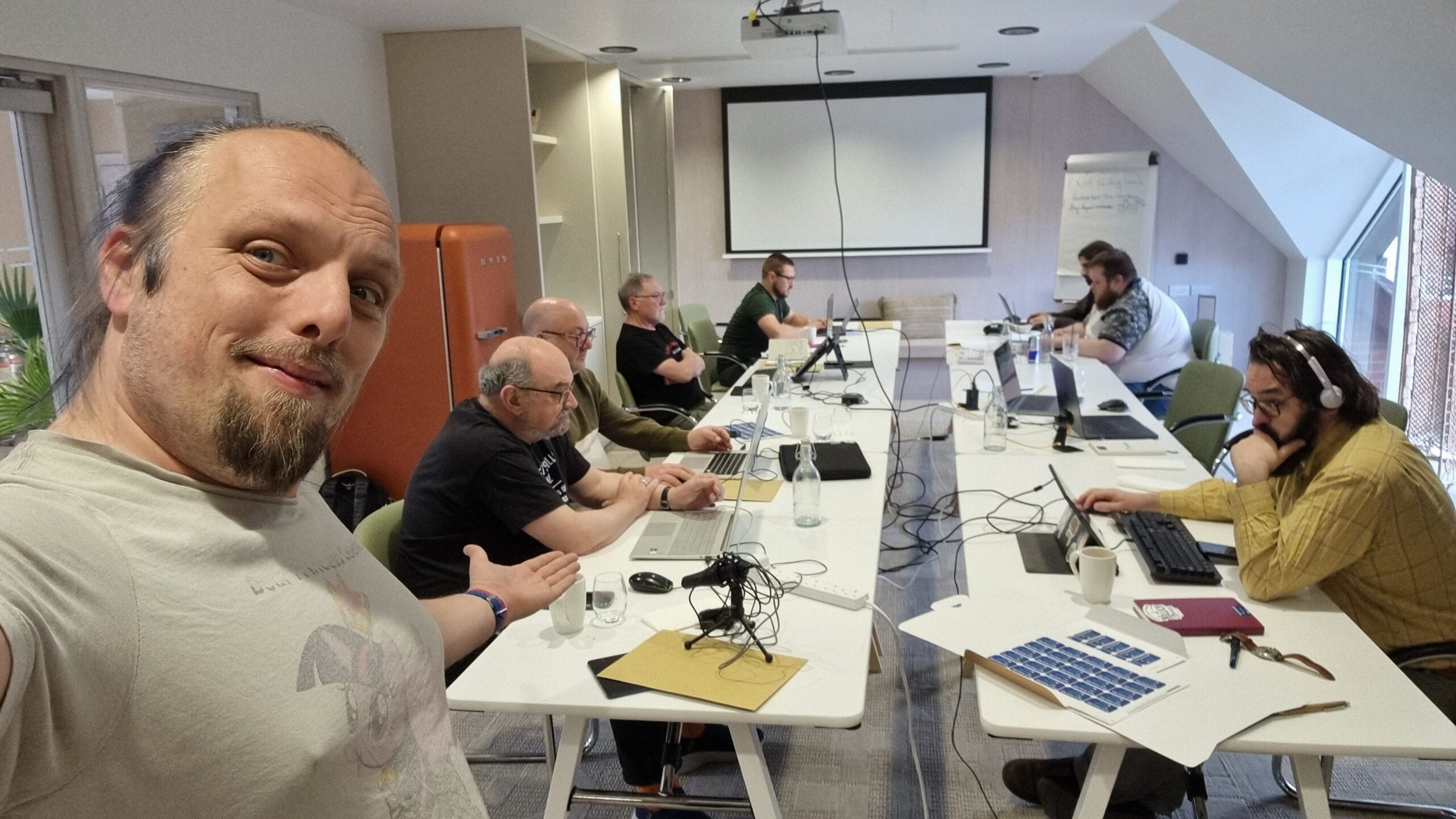 Full image of In a conference room, Dan stands in front of a group of people working on laptops.