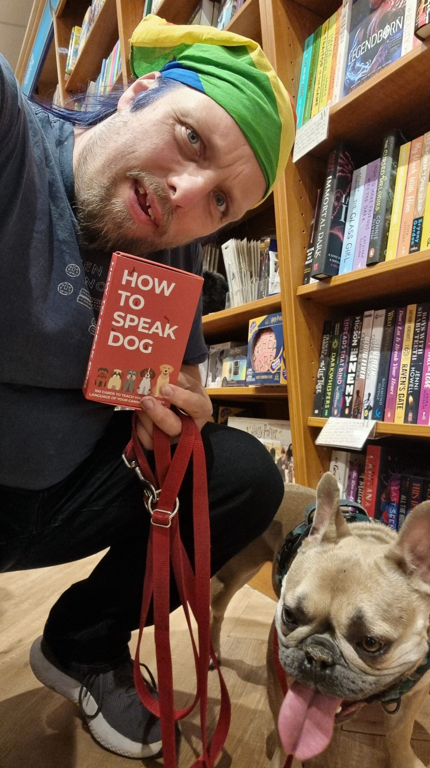 Full image of Dan, in a bookshop, holds a book called How To Speak Dog, alongside a French Bulldog.