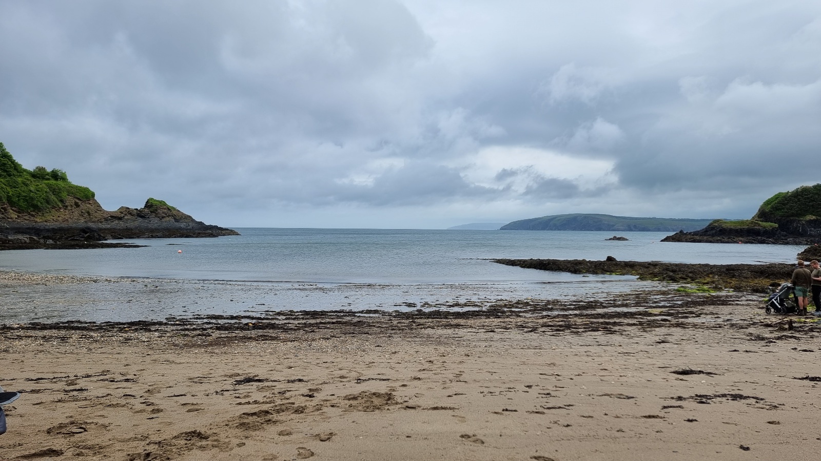 Full image of Sandy beach in front of a narrow bay, flanked by cliffs, under turbulent skies.