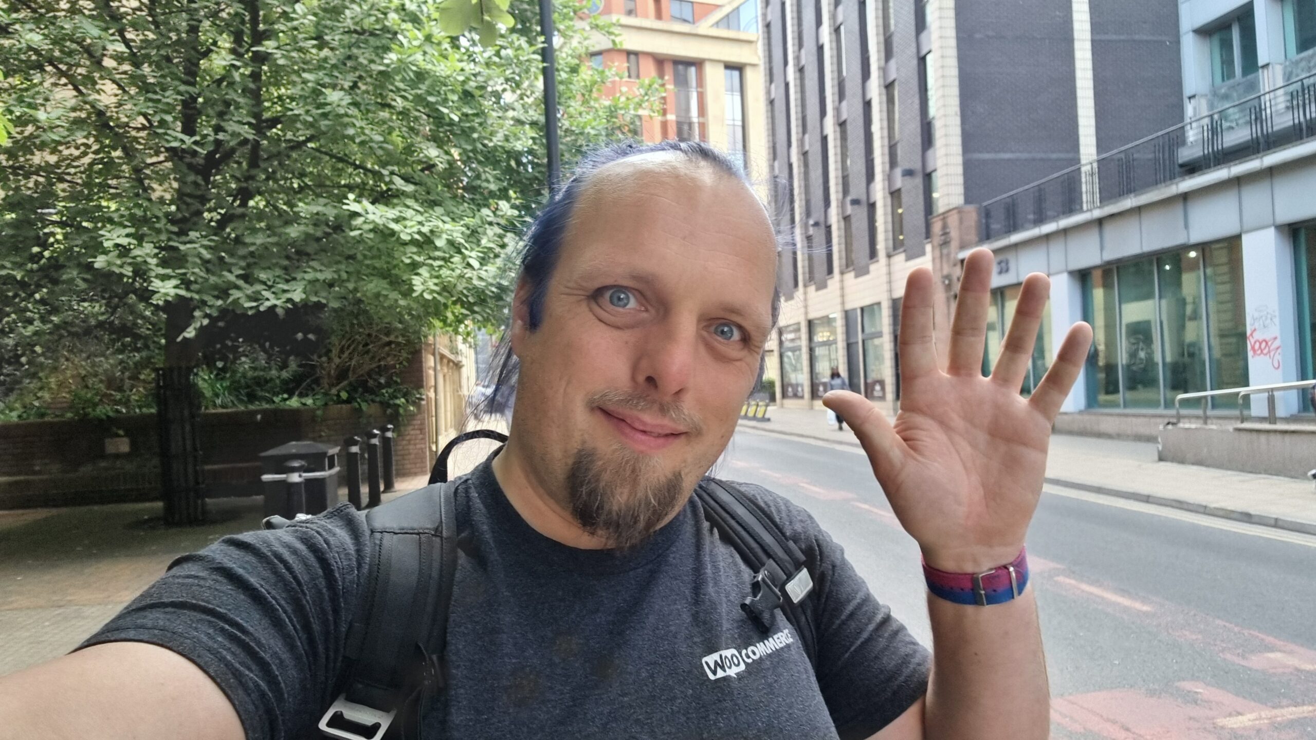 Full image of Dan waves from a leafy urban street.