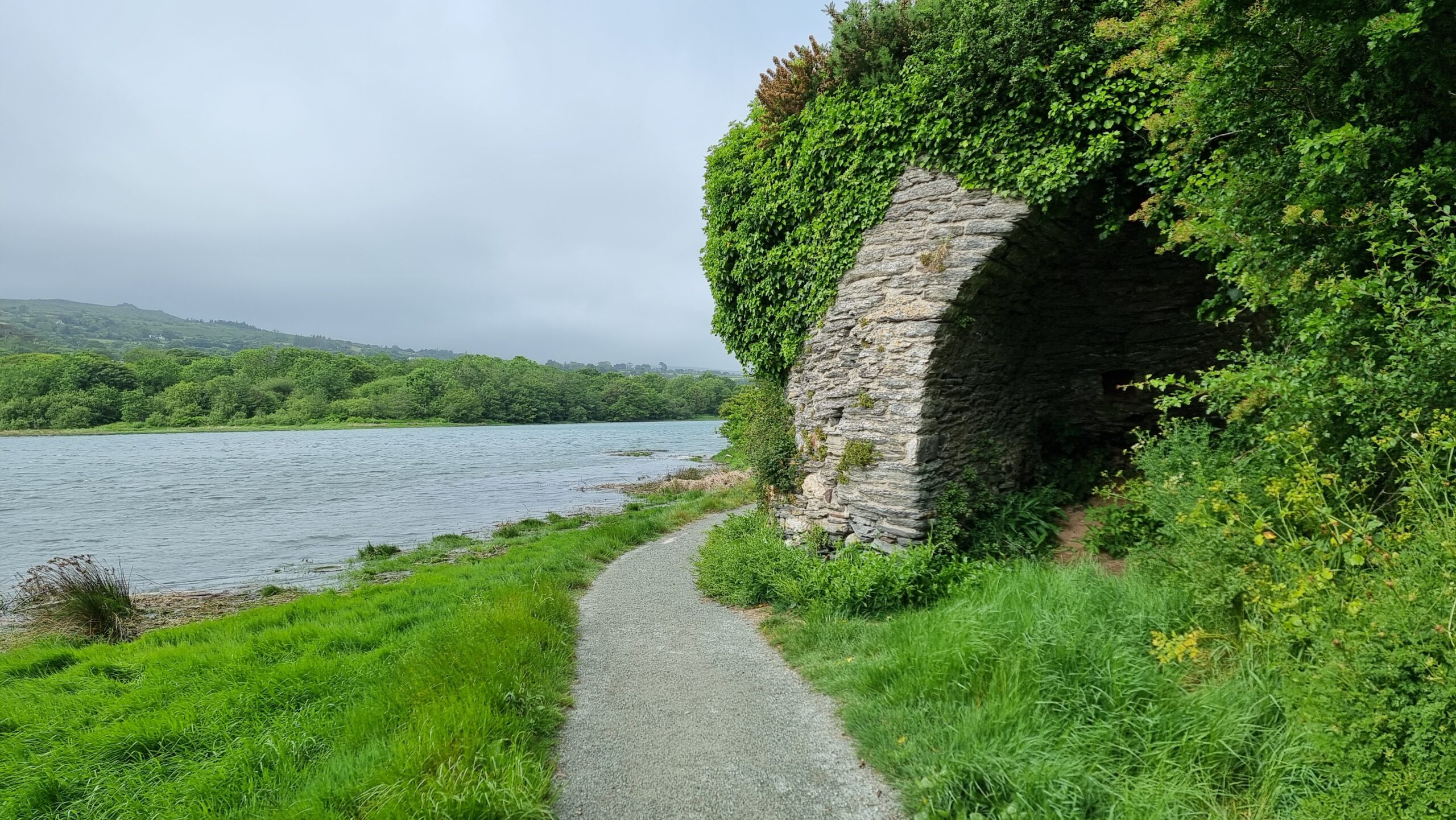 Full image of The remains of a stone kiln, a gravel path running alongside it, alongside a river estuary.