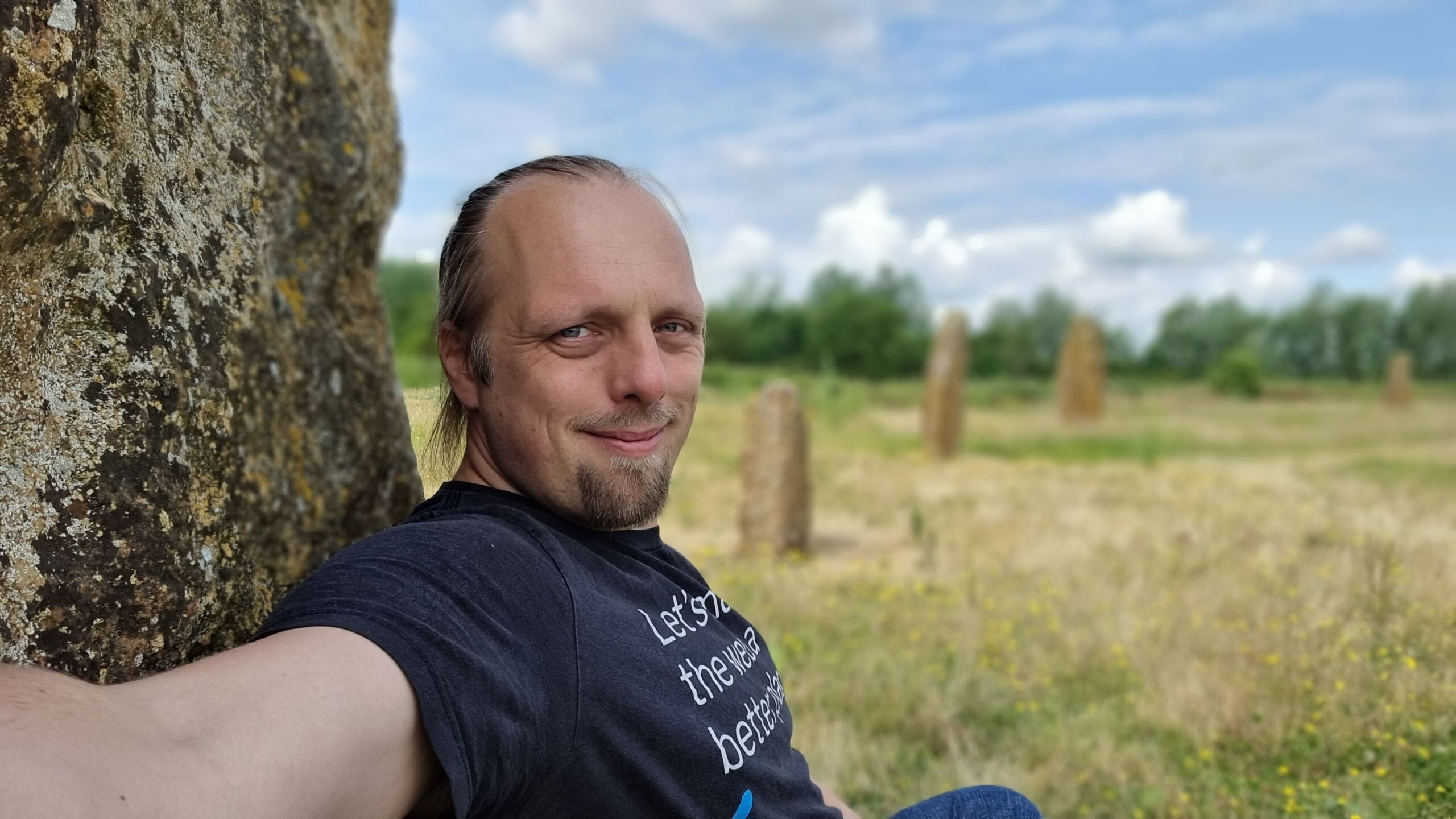 Full image of On a sunny day, Dan sits with his back to a stone, more of the circle visible in the background.