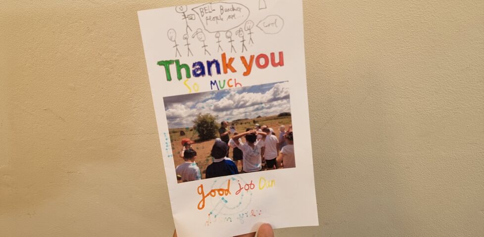 A hand-coloured card, saying 'Thank you so much', with a child's drawing of somebody talking about Bell Beaker people and a photo of Dan showing pictures of pots to a class of schoolchildren.