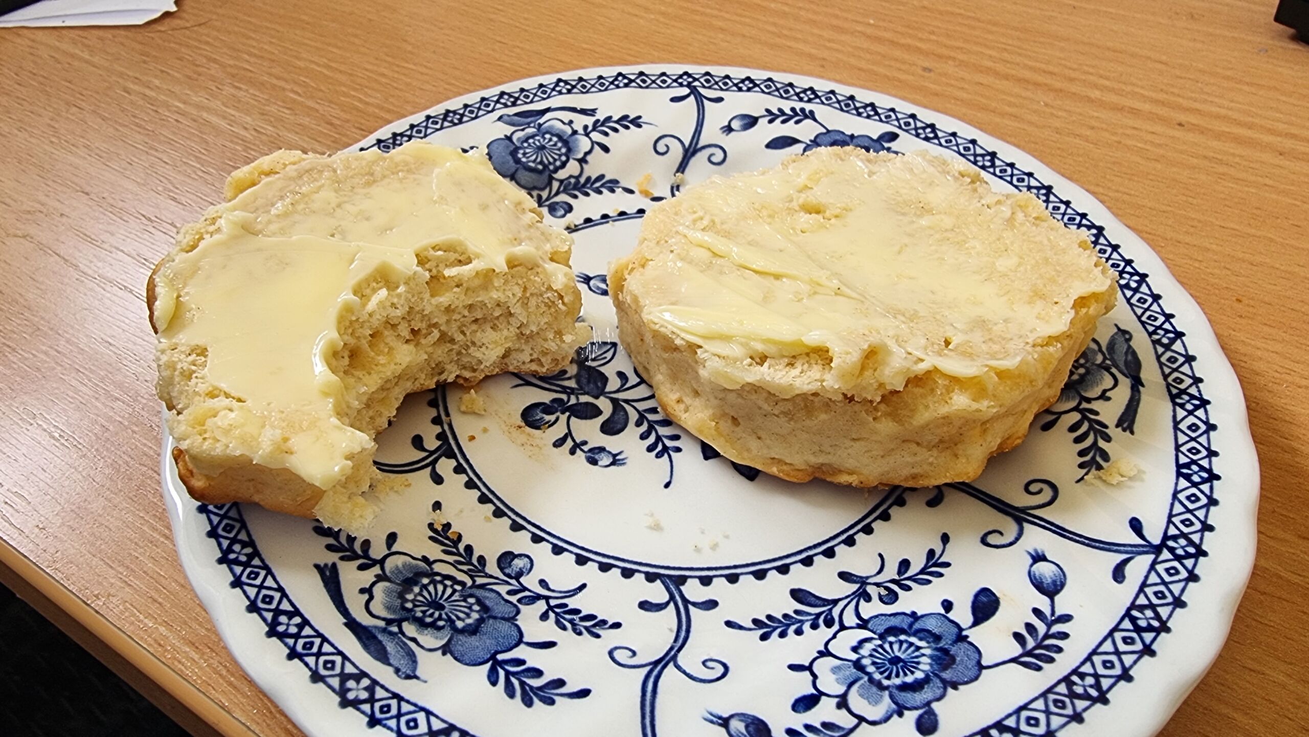 Full image of A crumbly hexagonal cheese scone, buttered, on a blue-and-white plate, with a single bite taken out of one half.