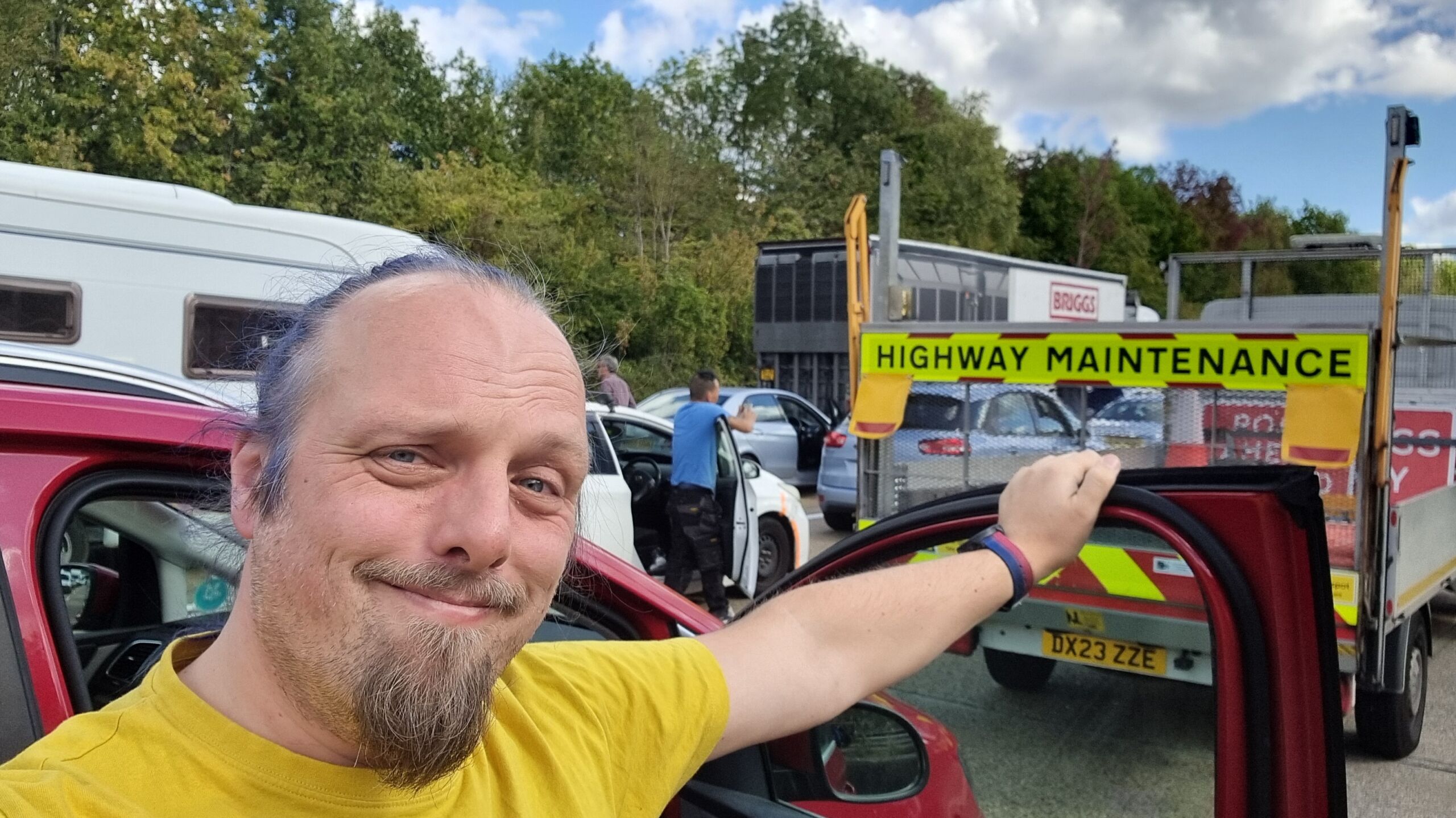 Full image of Dan stands among stationary cars and other frustrated drivers on a motorway.