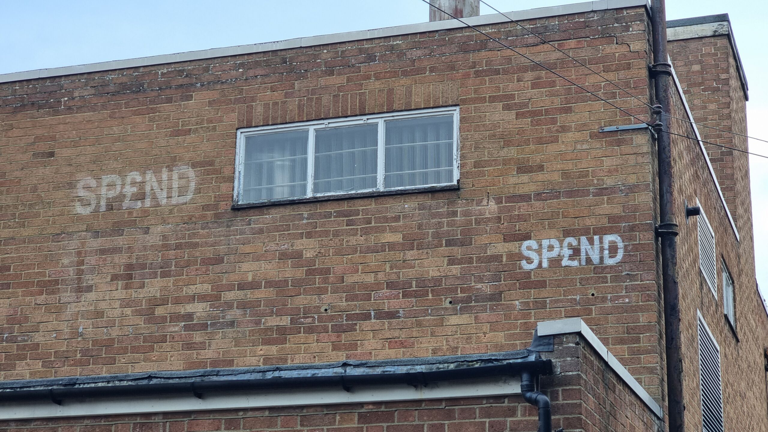 Full image of Brick building stencilled with SP£ND in two places.