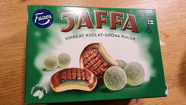 A box of Vihreät Kuulat Jaffa Cakes. The cross-section cutaway shows a green jelly within the biscuit, and alongside are pictures of spherical green jellies.