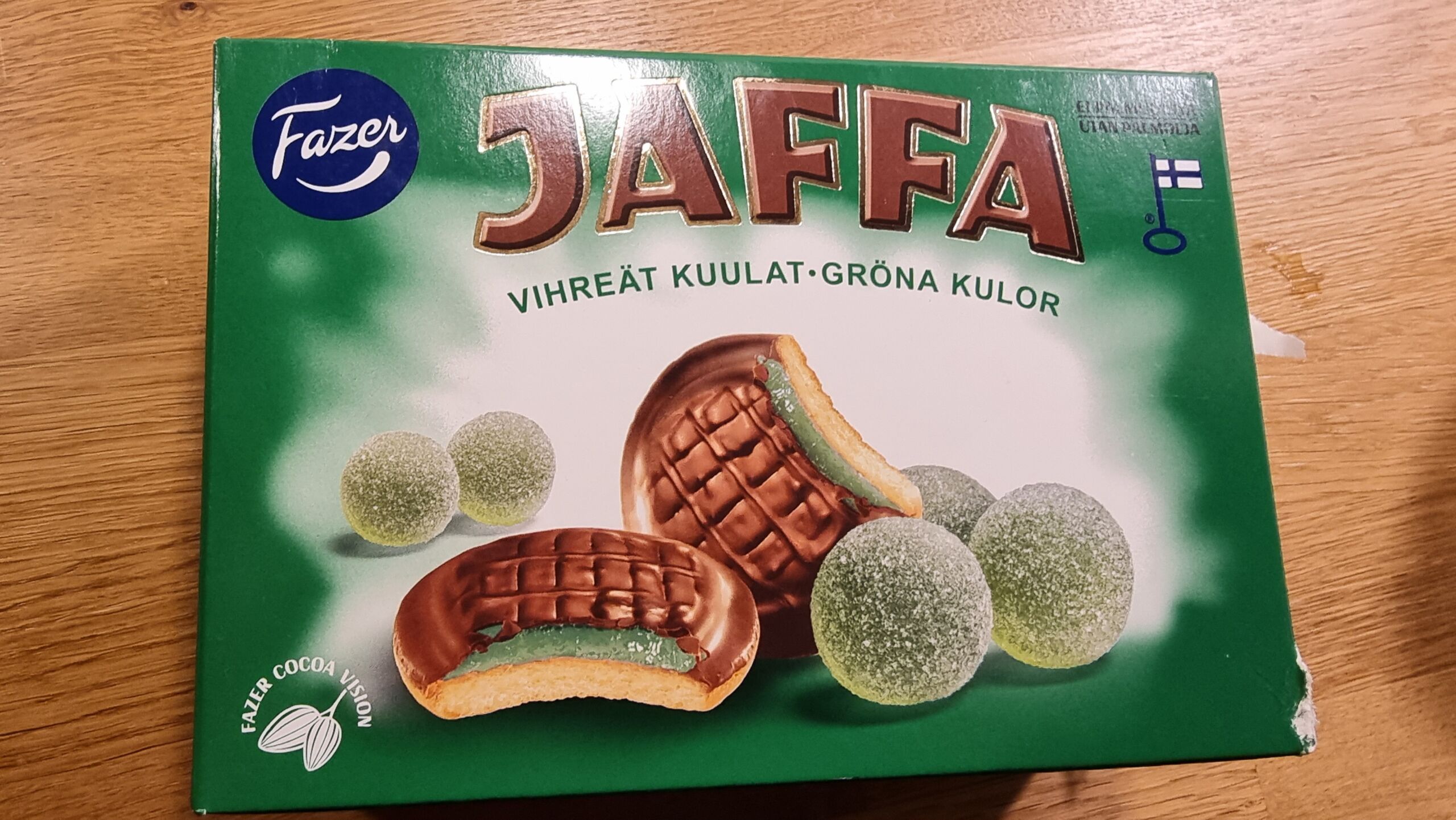 Full image of A box of Vihreät Kuulat Jaffa Cakes. The cross-section cutaway shows a green jelly within the biscuit, and alongside are pictures of spherical green jellies.