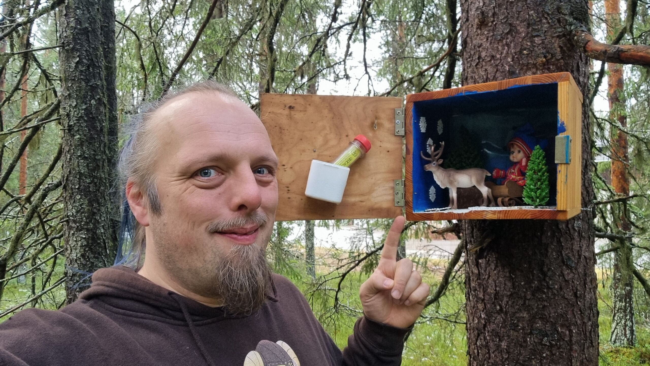 Full image of Dan points to an adorable Lapland scene installed in a wooden box attached to a tree.