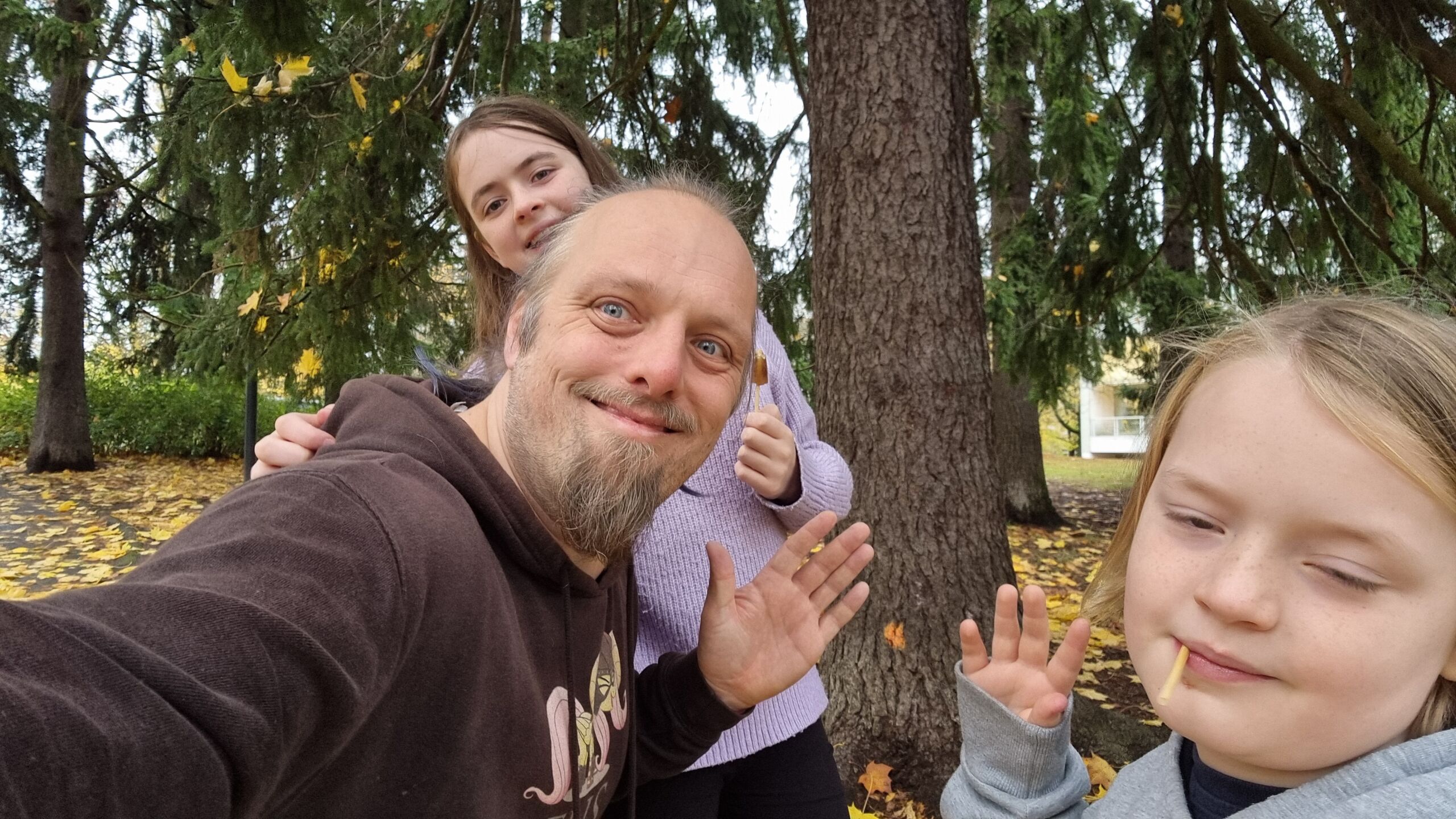 Full image of Dan and two children wave cheerfully from in front of a tree.