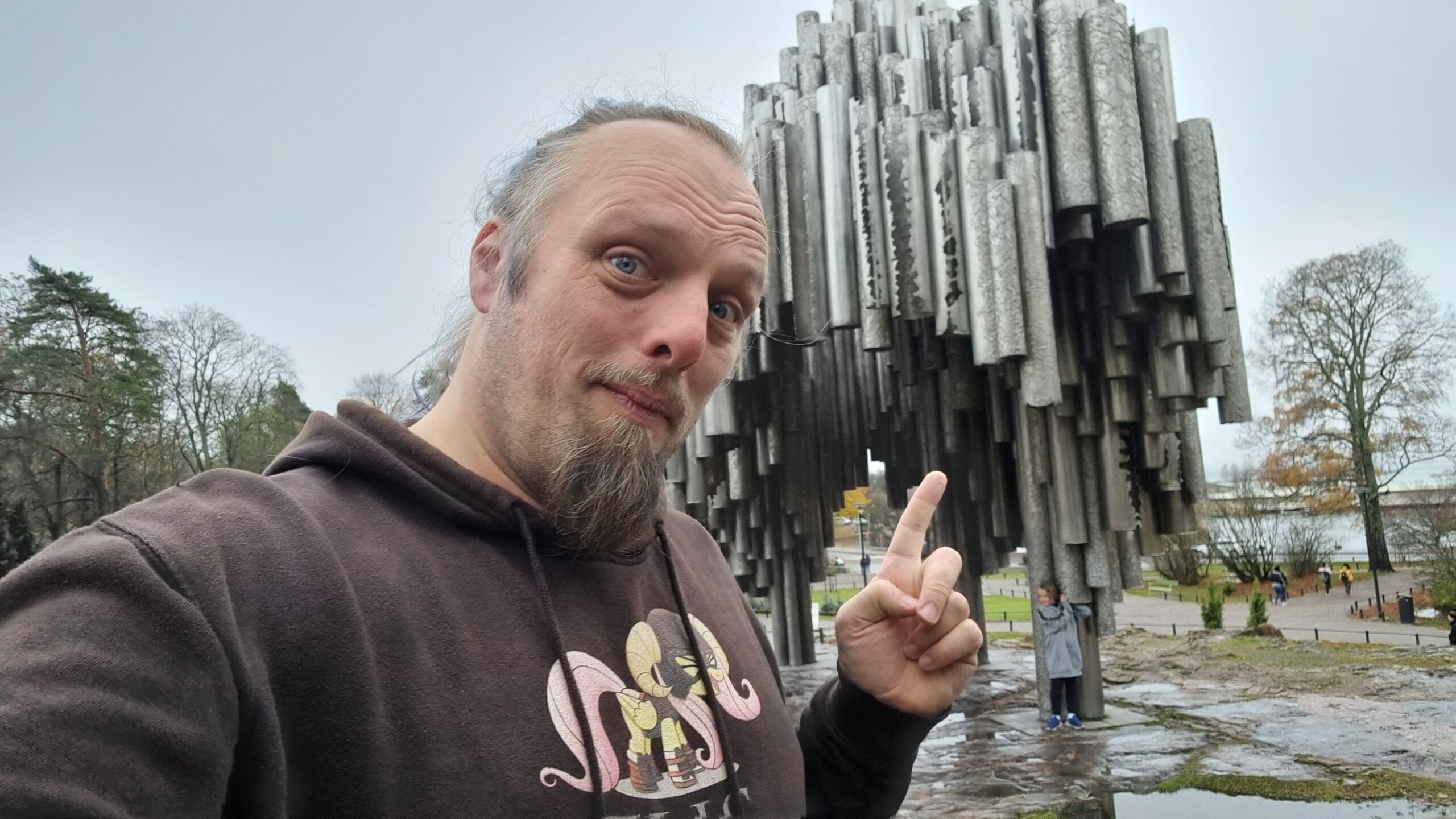 Full image of Dan points to an organic, tree-like sculpture formed from dozens of upright pipes.