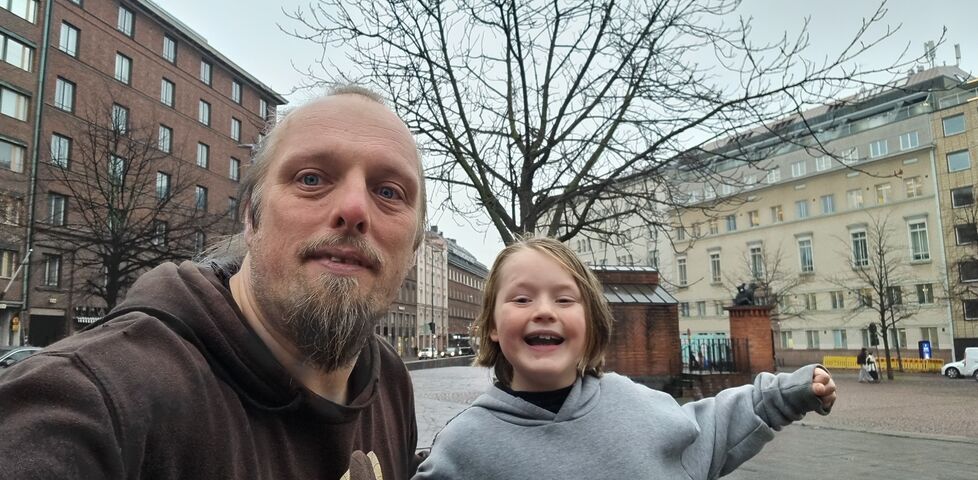 Dan and a young boy pose in front of a statue of two bears, atop a brick plinth in a city square.