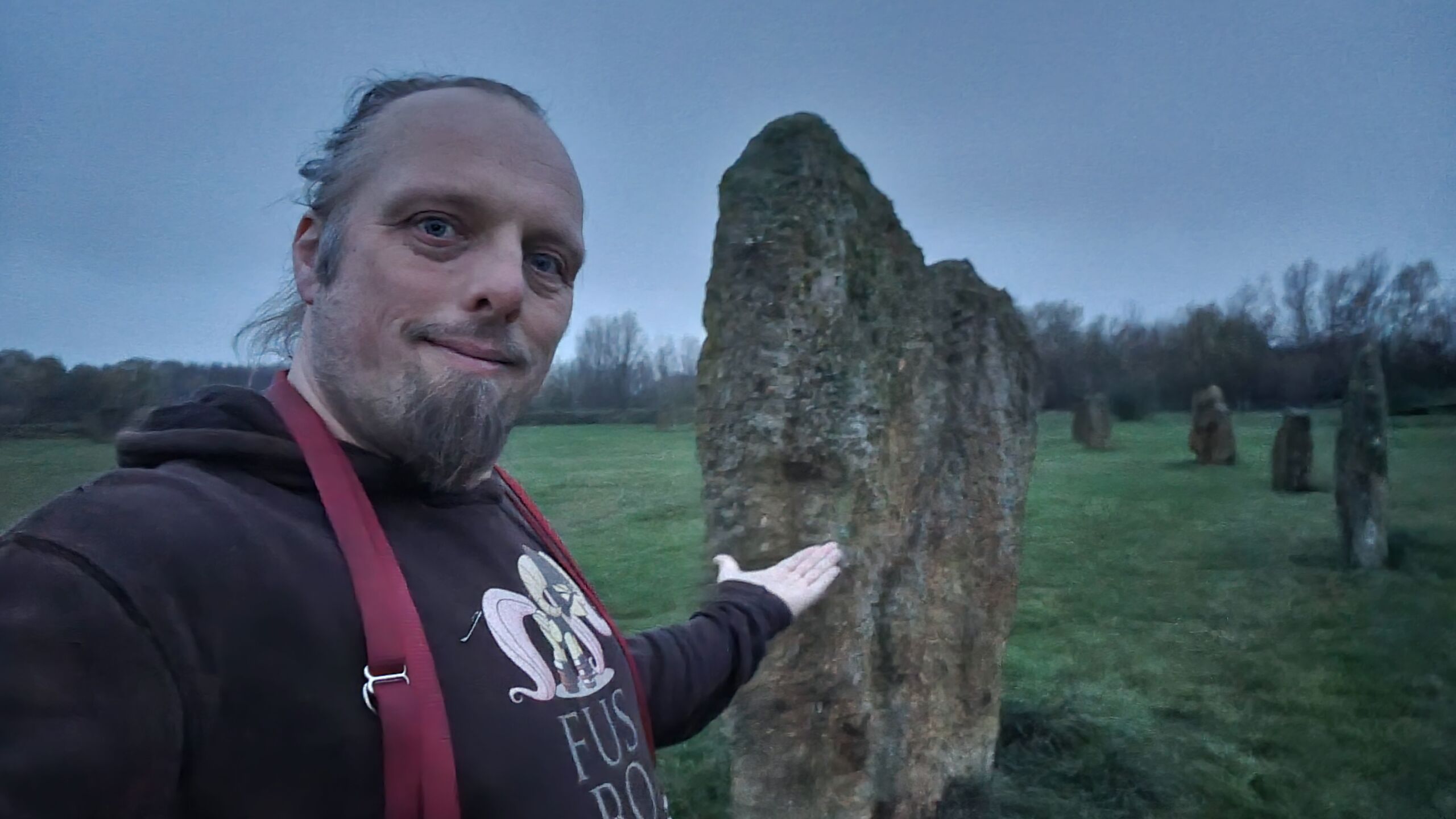 Full image of Dan in front of some standing stones at dusk.