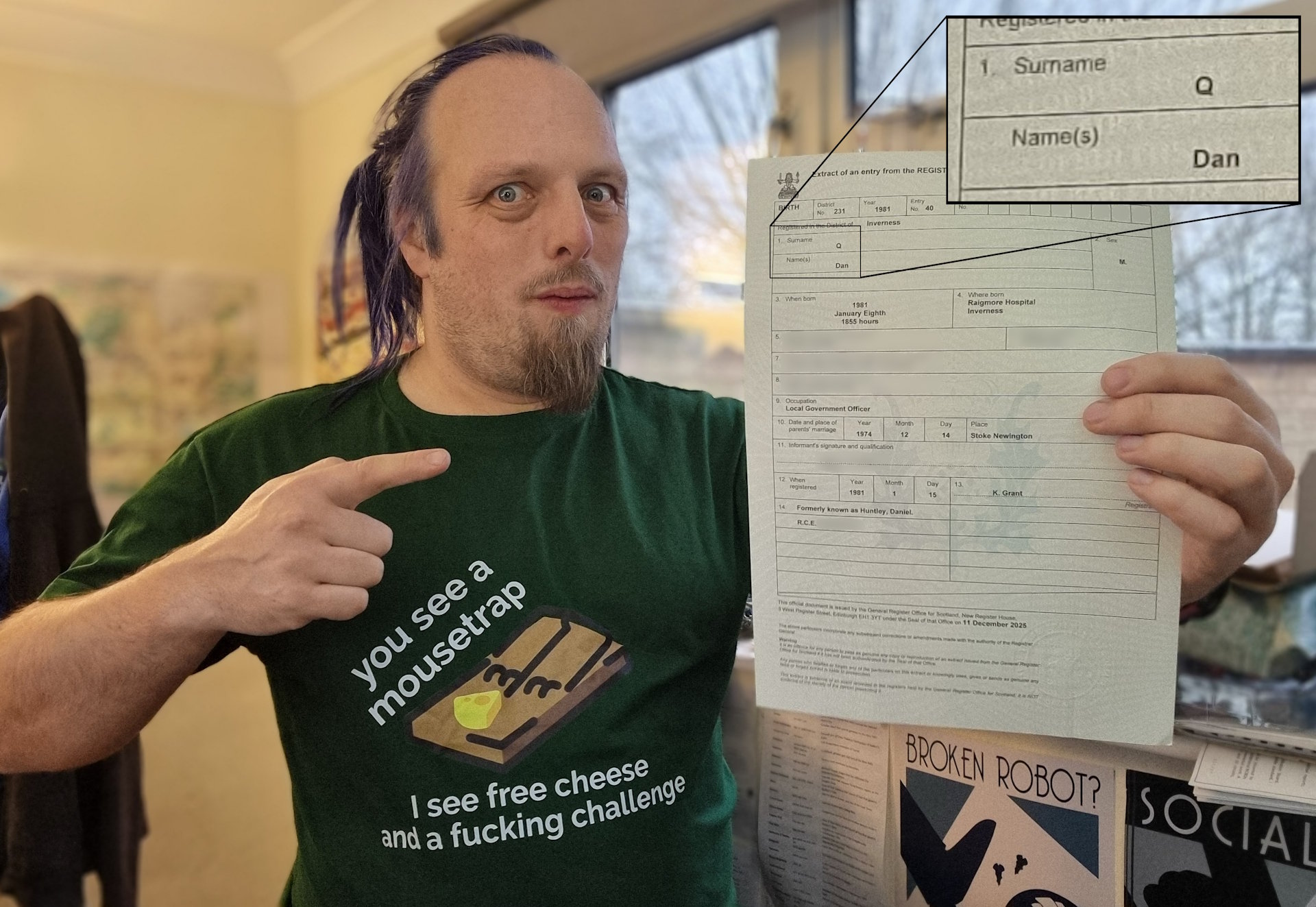 Full image of Dan, a white man with blue hair and a goatee beard, wearing a t-shirt reading 'you see a mousetrap, I see free cheese and a fucking challenge', holds up a Birth Certificate Extract on which his name appears as 'Dan Q'