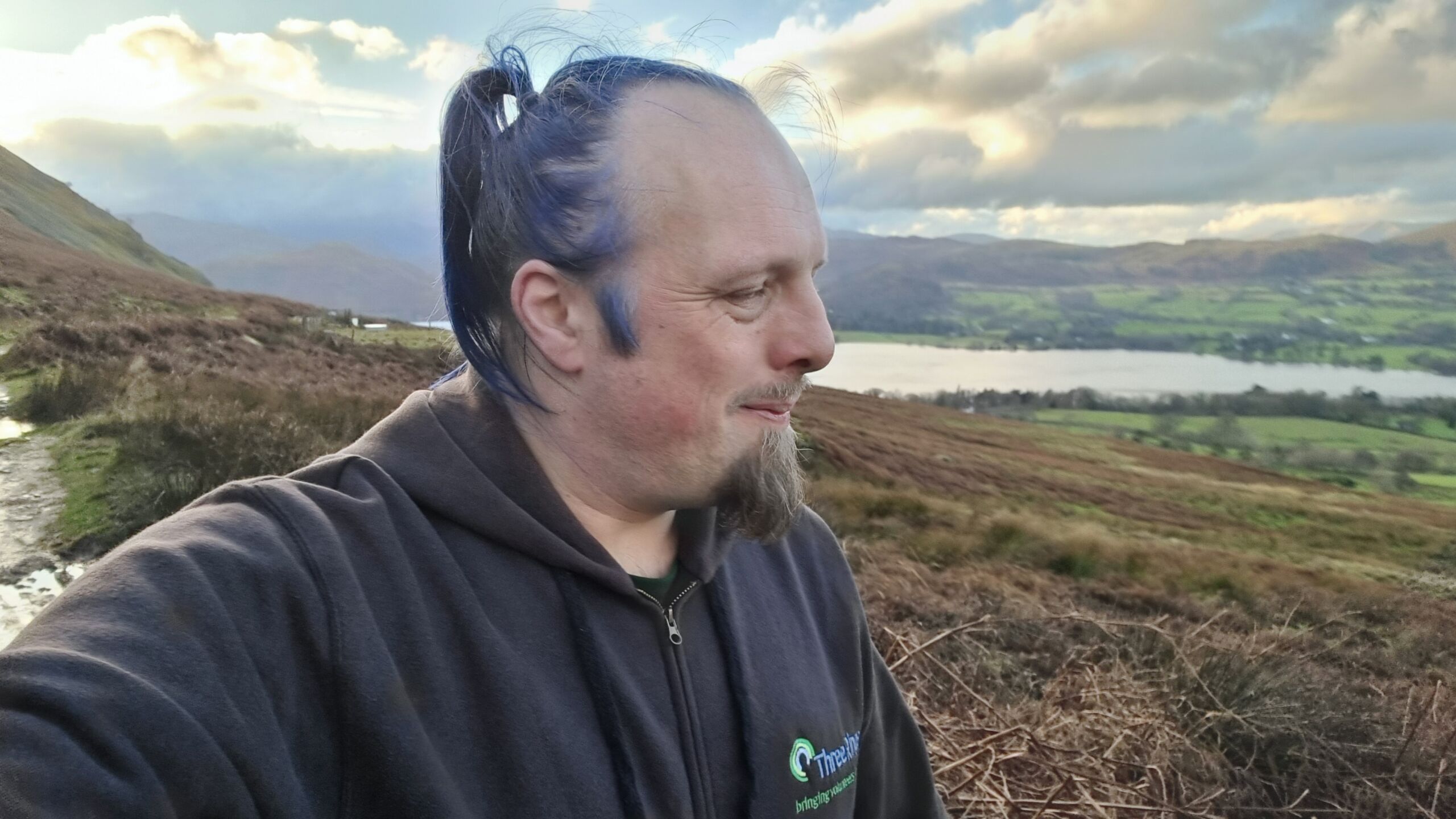 Full image of Dan, a white man with blue hair, looks over the valley of the Ullswater.