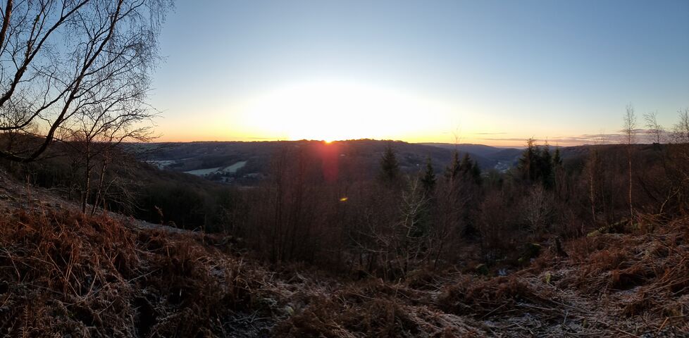 Sun rising over a hill beyond a broad valley full of frozen fields.