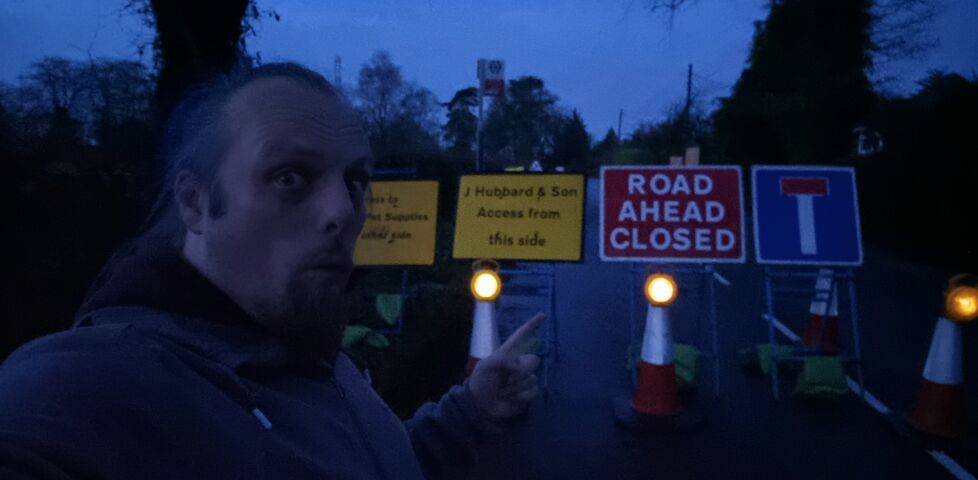 Dan, in the dark, stands in front of a number of road closure signs on a rural road.