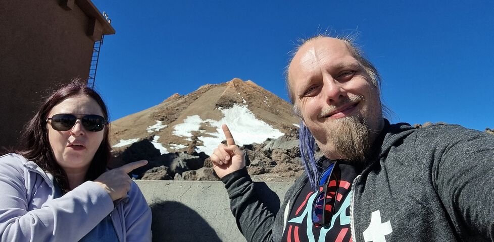 Dan and Ruth stand in front of a partially-snow-covered volcano cone.