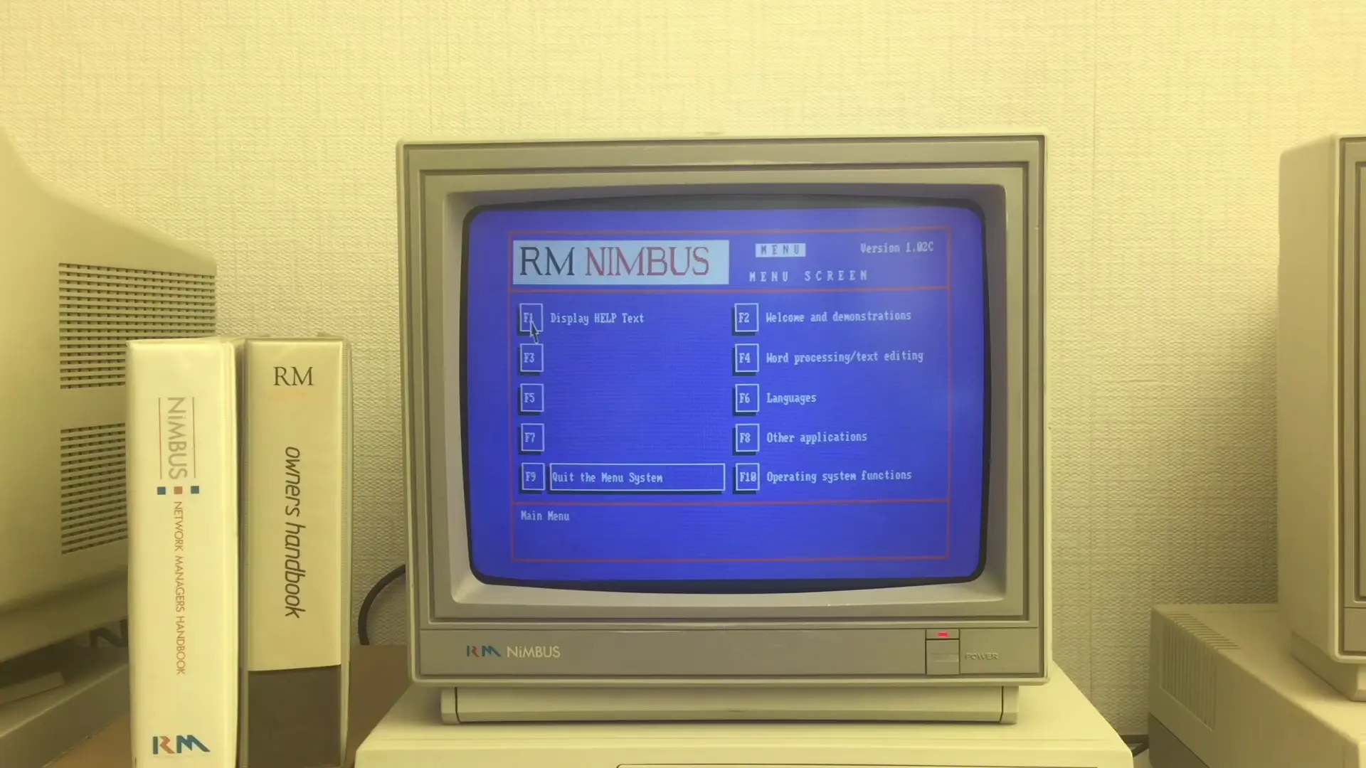 Full image of An RM Nimbus PC-186 at its launch menu; a DOS-based function key list menu to run a variety of different programs, alongside RM manuals.