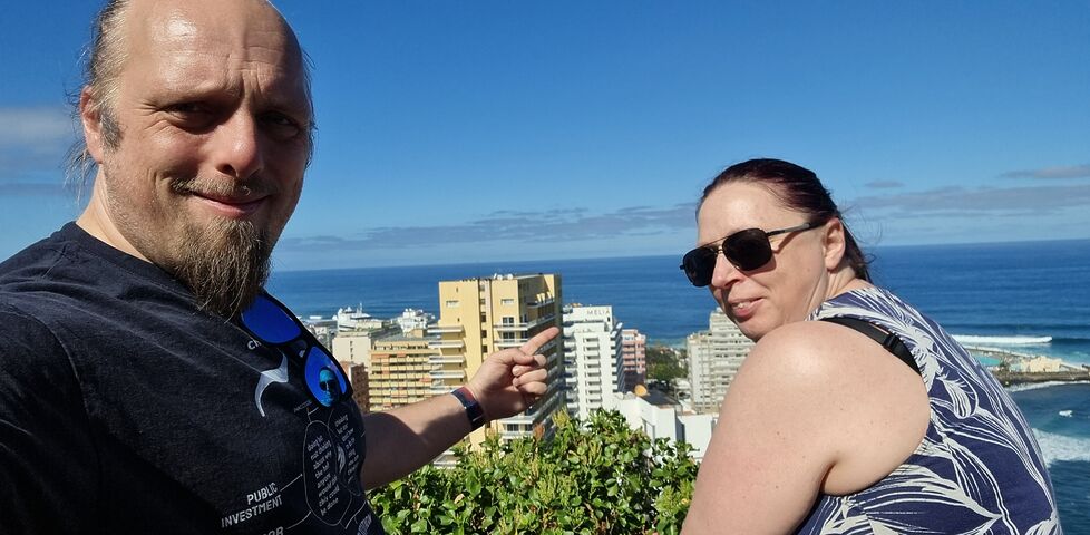 Dan and Ruth stand on an overlook, pointing at a seaside Meliá hotel in the distant city below.