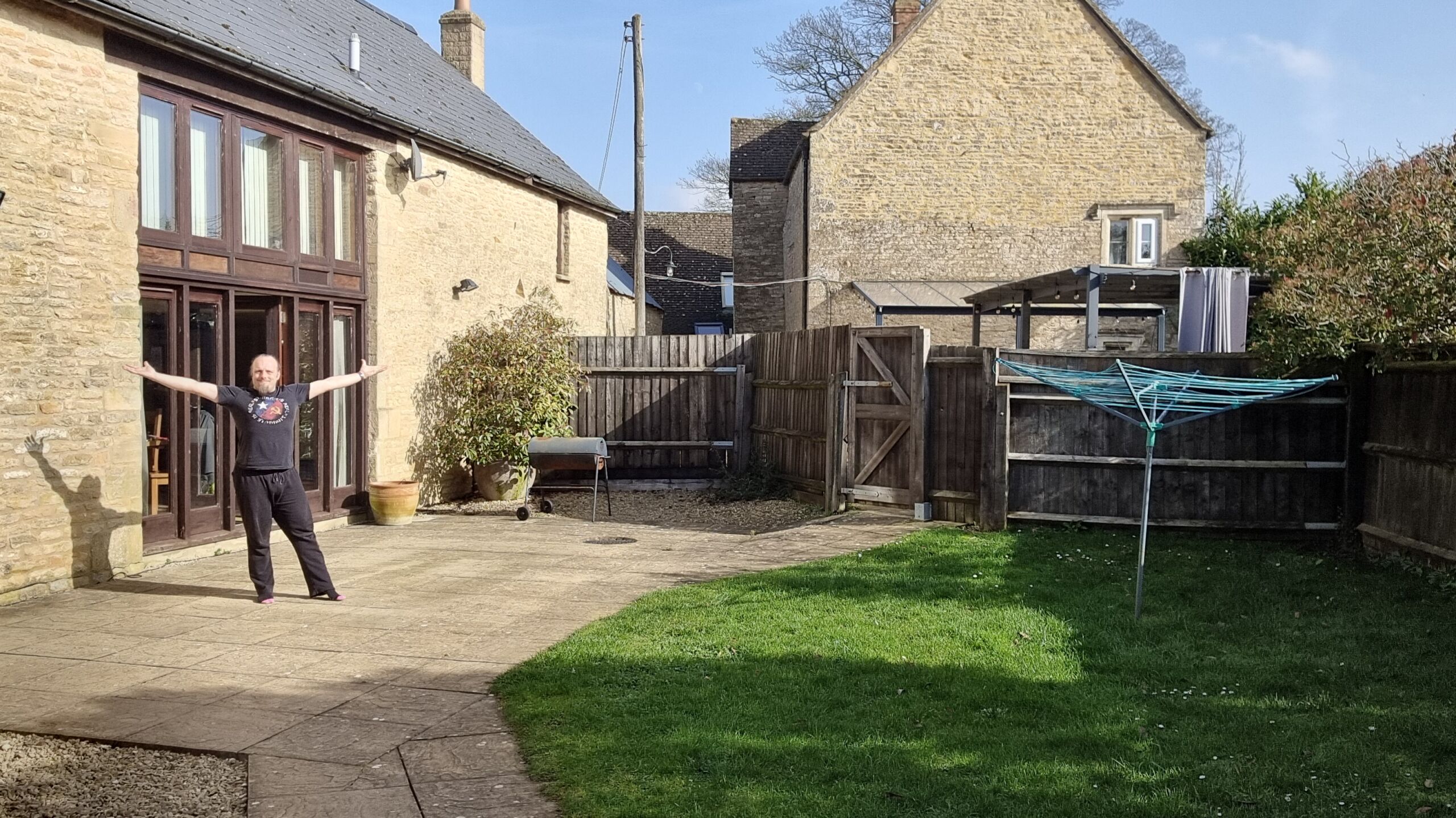 Full image of Dan, a white man, stands with his arms raised outside a nicely-decorated converted barn.