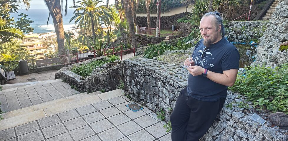 Dan leans against a wall in a tropical park, writing on a log sheet.