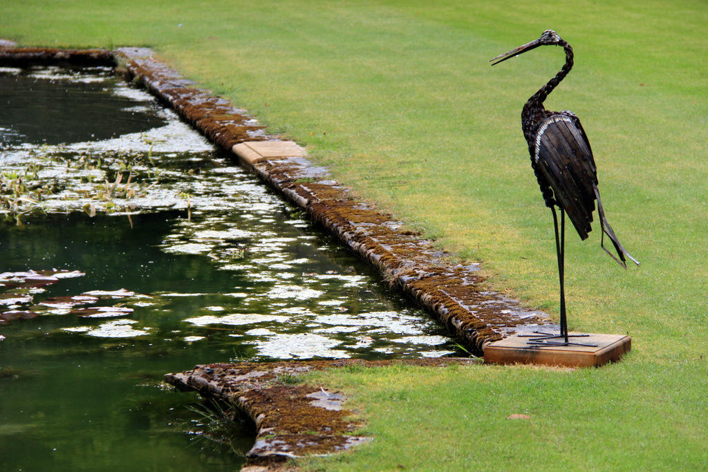 Full image of Metalwork fake heron alongside a manicured pond.