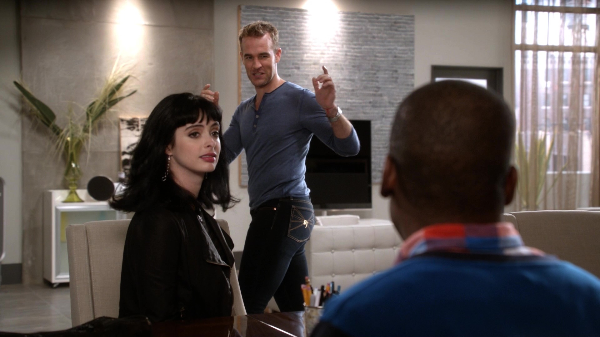 Full image of Chloe (Krysten Ritter) speaks to Luther (Ray Ford) across a desk, while James Van Der Beek - playing a fictionalised version of himself - poses in the background to show off the jeans he's wearing.