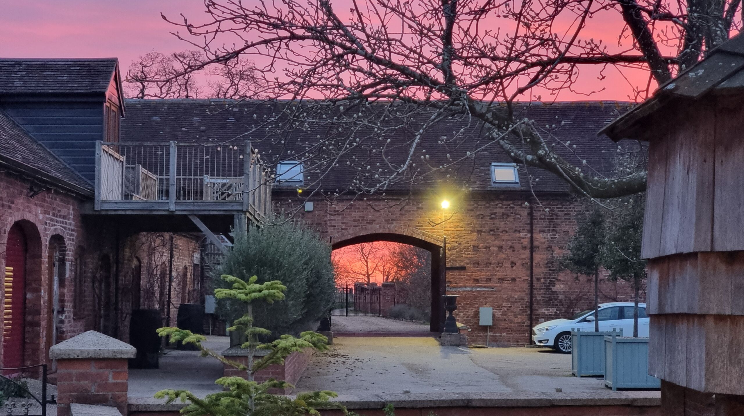 Full image of The sunrise as seen through the gates of a vineyard's courtyard.