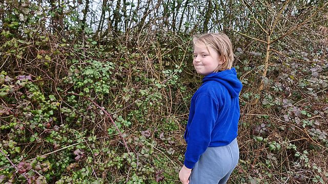 A boy looks over his shoulder as be begins to walk into a bramble bush.